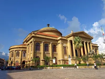 a large yellow building with palm trees in front of it at Il Cavaliere Apartment in Capaci