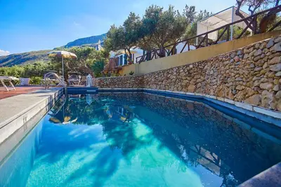 a swimming pool with blue water and a stone wall at Villa Lo Zingaro - Scopello-Villas in Scopello