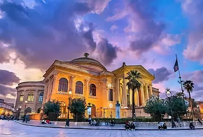 a large yellow building with palm trees in front of it at Bieddu Suites - Palermo City Center in Palermo