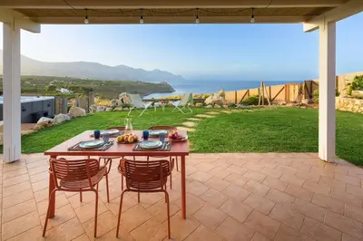 a table and chairs on a patio with a view of the ocean at Villa Faraglioni Cala Bianca in Castellammare del Golfo