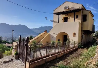 a house with a fence and mountains in the background at Casale di Sicilia in Monreale