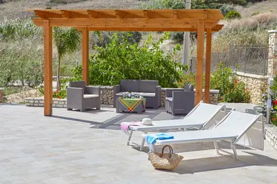 a patio with white lounge chairs and a wooden pergola at Villa Ninetta in Scopello
