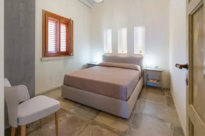 a bedroom with a bed and a chair and a window at Villa Zingaro Cala Bianca in Castellammare del Golfo