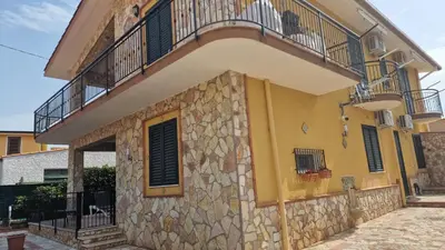 a yellow building with a balcony and a stone wall at Villino Giovanna a Trabia a 200 mt dal mare in Trabia