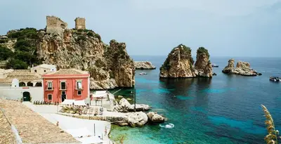 a red building in the water next to the ocean at Villa Capreria by Sicily Travelling Villas in Scopello