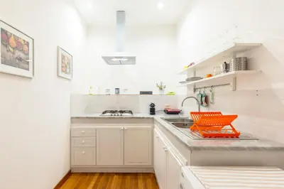 a white kitchen with an orange chair on the counter at Piazza Marina Holiday House by DomuSicily in Palermo