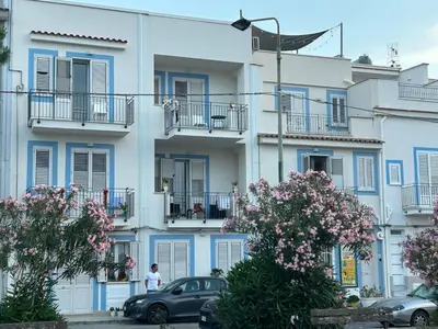 a building with blue shutters and cars parked in front at Finestra del mare in Isola delle Femmine