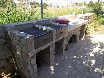 a stone barbecue grill in a yard with a fence at Casa vacanze mare Rosa in Castellammare del Golfo