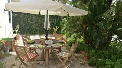 a table and chairs under an umbrella in a garden at B&B Ondamarina in Lascari