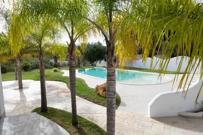 a pool with palm trees and a dog laying next to it at Le Onde della Sicciara in Balestrate