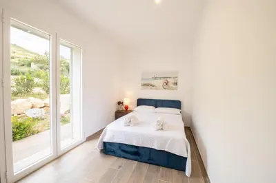a white bedroom with a bed and a large window at Villa Manù country house in Castellammare del Golfo