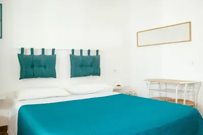 a white bedroom with a blue bed with blue pillows at Villa Torre Ulisse Locazione Turistica Affitti Brevi in Carini