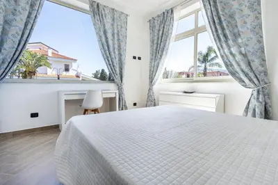 a white bedroom with a bed and two windows at Villa Sandoval in Palermo