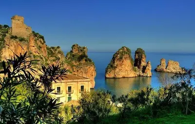 a building in the middle of the water with some rocks at Scopello Beach in Scopello