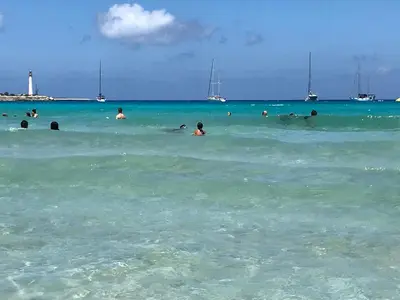 a group of people swimming in the ocean with a lighthouse at euforbia in San Vito lo Capo