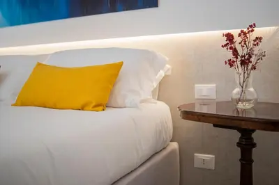 a white bed with a yellow pillow and a table at Dimora Ballarò in Palermo