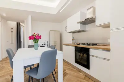 a white kitchen with a white table and chairs at GuestHost - Hamuri Holiday House - Heart of Palermo in Palermo