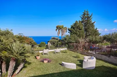 a garden with white chairs and a view of the ocean at Villa Pandora in Scopello