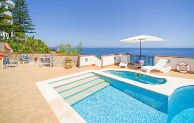 a blue swimming pool with an umbrella and the ocean at Nice Home In Altavilla Milicia in Altavilla Milicia