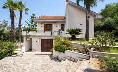 a white house with palm trees and a driveway at Villa Viola e Giulio in Scopello