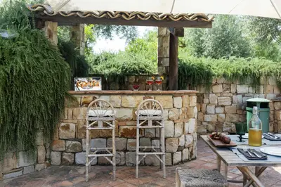 an outdoor bar in a stone wall with two stools at Villa Passulunara 14 by Massimo Villas in Lascari