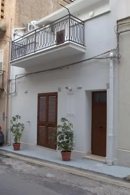 a white building with a balcony and two plants at Bom Bom Apartments in Castellammare del Golfo
