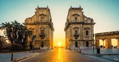 two buildings on a street with the sunset in the background at Manuè's House in Palermo