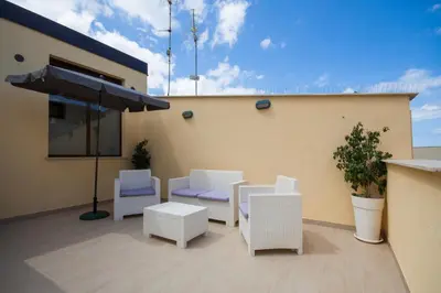 a patio with white chairs and an umbrella at Casa Vacanze del Golfo in Castellammare del Golfo