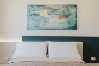 a painting above a bed with two white pillows at Villa con Piscina in Balestrate