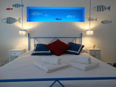 a bed with white sheets and blue and red pillows at La Maschera di Giano, case vacanza vista mare in Palermo