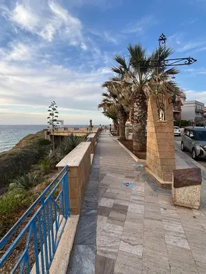 a sidewalk next to the ocean with palm trees at Casa Miramara Sicilia in Balestrate