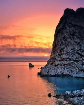 a sunset over the ocean with a large rock formation at Villino Rosa in Santa Flavia