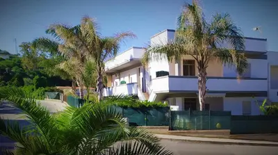 a white building with palm trees in front of it at MuSa Apartament in Balestrate