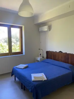a bedroom with a bed with blue sheets and a window at I Carrubi in Lascari