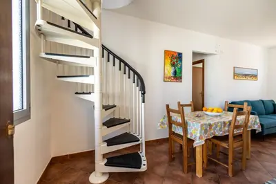 a dining room with a table and a spiral staircase at Appartamenti da Lulù in San Vito lo Capo