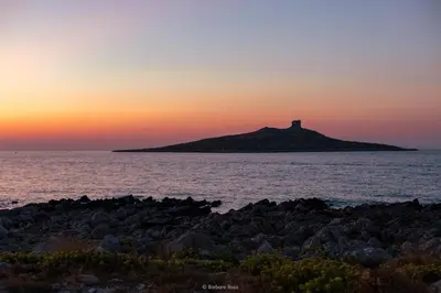 a lighthouse on an island in the ocean at sunset at Cavalluccio Marino Holiday in Isola delle Femmine