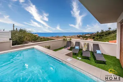 a swimming pool with chairs and a view of the ocean at Appartamenti in villa Ionio vista mare con piscina riscaldata e campo da bocce in Alcamo