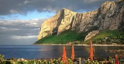 a mountain next to a body of water with red flowers at Casa Cavarretta in Palermo