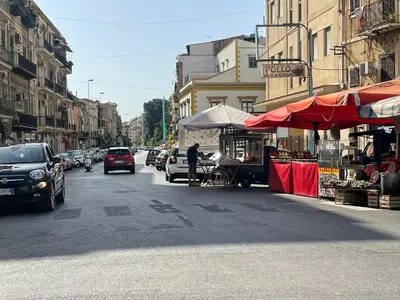 a street with cars driving down a city street with a market at Appartamento la Noce in Palermo