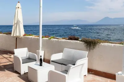 a patio with white chairs and a table and an umbrella at Casetta Bianca Luxury in Santa Flavia