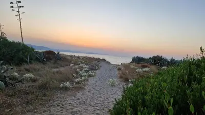 a sandy path leading to the ocean at sunset at a due passi dal mare in Campofelice di Roccella