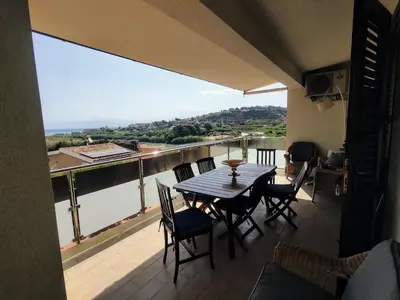 a table and chairs on a balcony with a view of a river at Cas'aMare Holidays, Home is Love in Castellammare del Golfo
