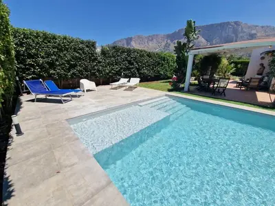 a swimming pool with two blue chairs and a house at Villa indipendente con piscina in Terrasini
