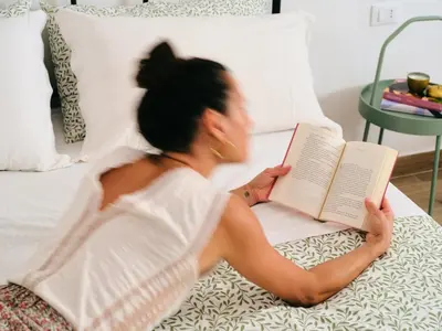 a woman laying on a bed reading a book at La casa di giù in Palermo