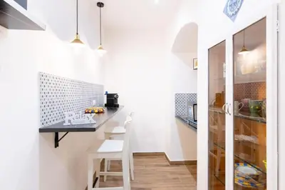 a kitchen with white walls and a black counter and white chairs at Balarm-Boutique Rooms in Palermo