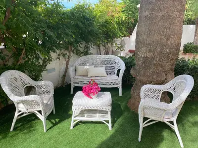 three white wicker chairs and a table with flowers on it at Villa Glicine a pochi passi dal mare e dal centro in San Vito lo Capo
