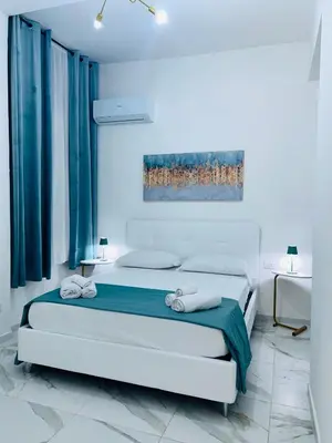 a white bedroom with a bed with blue curtains at Coco Memi Apartment in Palermo