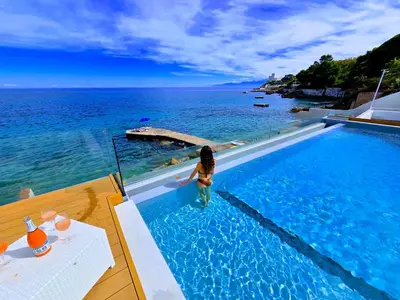a woman standing in a swimming pool overlooking the ocean at White Coral in Santa Flavia