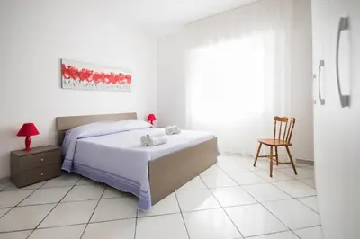 a white bedroom with a bed and a chair at Villa Cielo d'Alcamo Marina in Alcamo