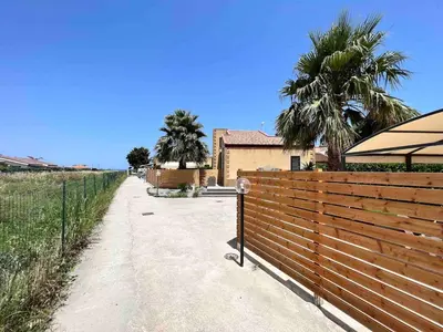 a fence next to a house with palm trees at Villa Stromboli - Le Ville del Mediterraneo in Campofelice di Roccella